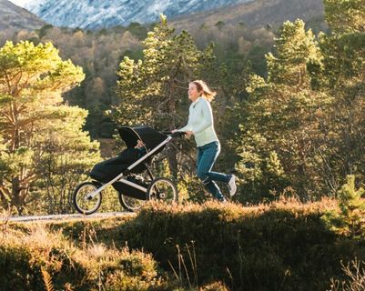A woman runs through a sunny country trail with the best running stroller from Thule.