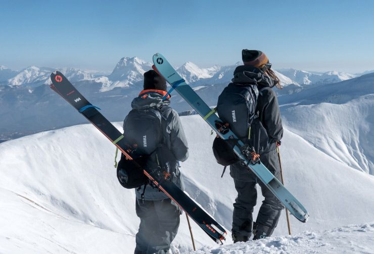 Alice Linari and Lorenzo Alesi stand on a snowy mountain looking at the view with skis and Thule ski backpacks.