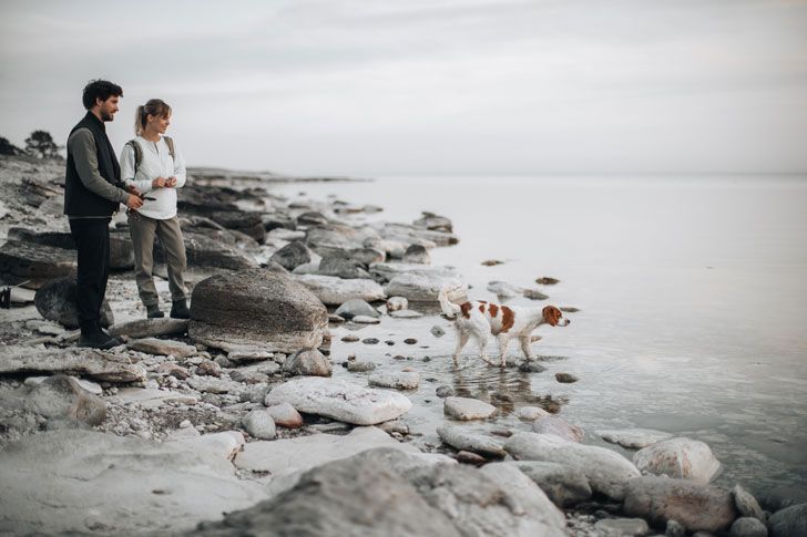 Ein Mann und eine Frau betrachten ihren Hund am Ufer des Wassers.
