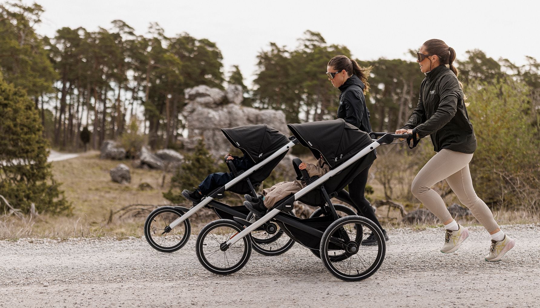 Zwei Erwachsene laufen mit Kindern in Thule Glide 3 Laufkinderwagen.