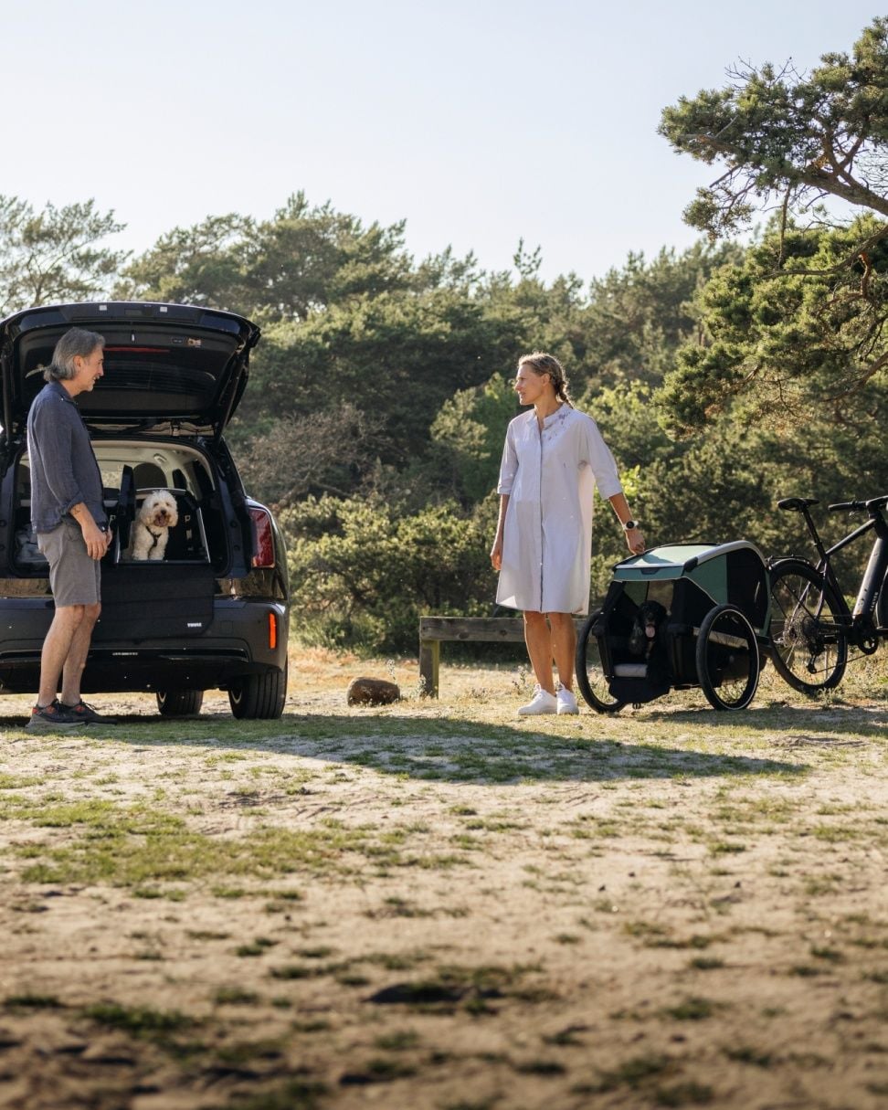 一男一女站在汽車後方，一隻狗坐在 Thule Allax 狗籠中，籠門敞開。
