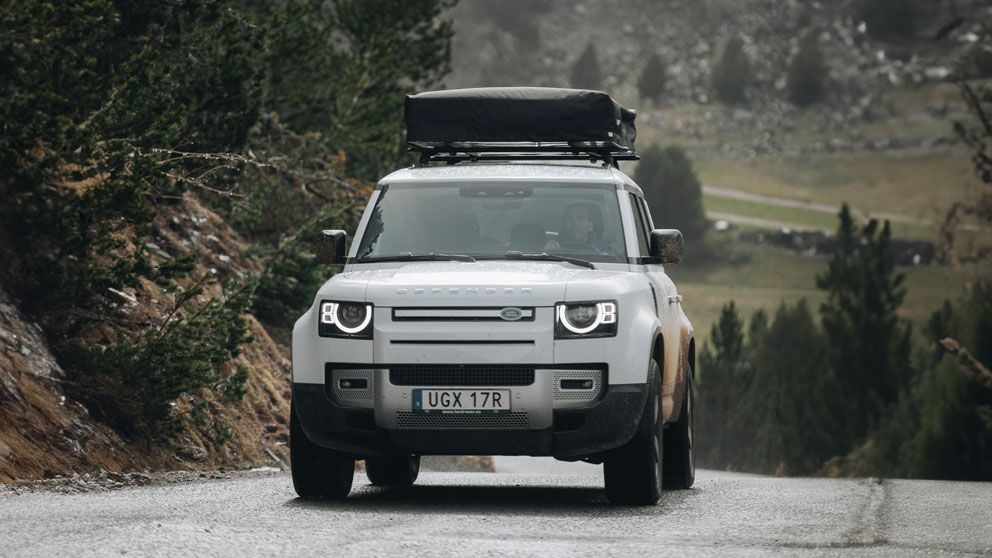 Ulicą jedzie Land Rover Defender ze złożonym namiotem dachowym na bagażniku bazowym.