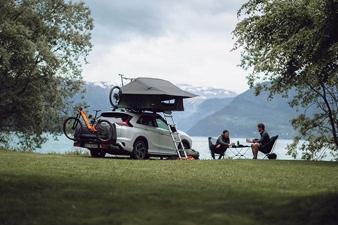 A car with a rooftop tent is parked by a lake wth a rear cargo carrier solution for EVs.