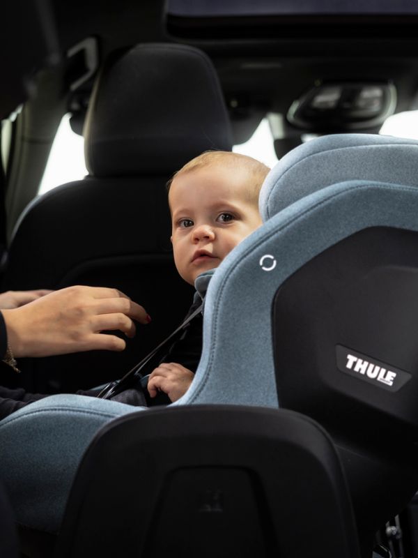 一个婴儿坐在浅灰色的 Thule Elm 幼儿汽车座椅上。一个人的手放在幼儿的安全带旁边。