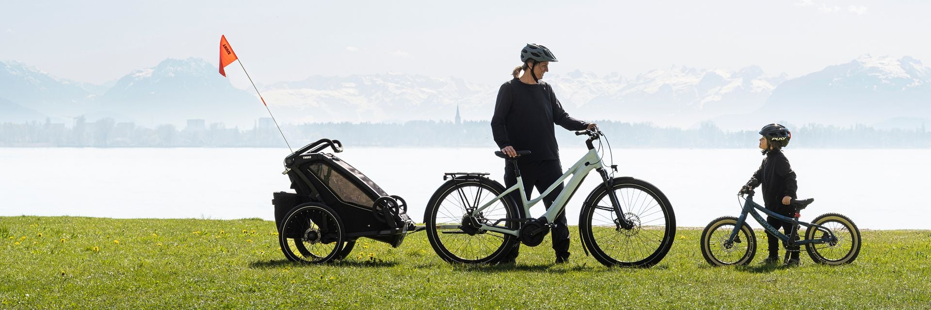 Un parent faisant du vélo avec une caravane d’enfant dans un cadre naturel.