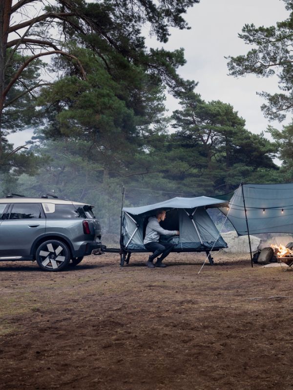 Thule Outset-biltelt i en leirplass i skogen, koblet til et kjøretøy med synlig tilbehør som tarp og campingutstyr