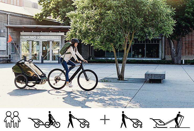 A woman bikes down a city street with the Thule Chariot Cab bike trailer