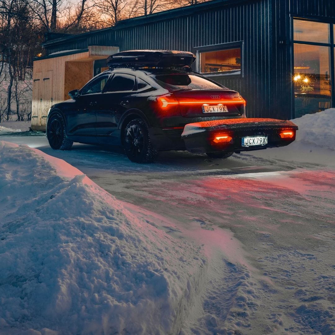 Coche equipado con cofre de techo Thule y Thule Arcos XL, estacionado en un paisaje invernal nevado.