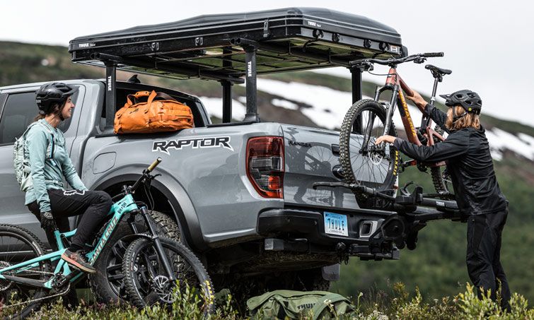 In nature a cyclist loads their Thule T2 Pro XTR hitch bike rack installed on a pickup.