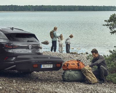 Un véhicule est stationné sur la plage avec un porte-bagage sur attache-remorque tandis qu’une famille se tient à côté.