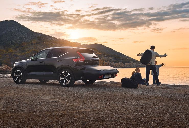 Durante el atardecer, una familia estaciona a la orilla del agua con un automóvil que tiene un baúl de carga Thule Arcos.