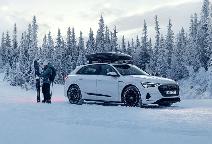 Un homme prépare ses skis à côté d'un véhicule électrique avec coffre de toit.