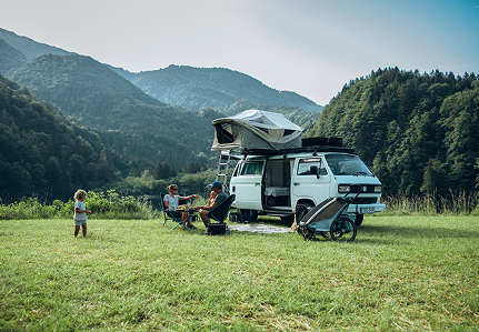 Les gens discutent autour d’un camping-car avec une tente Thule sur le toit et une remorque Thule à vélo à côté. 