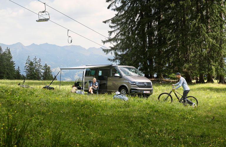 A compact van is parked under cable cars, and a woman sits under the Thule Sidehill awning.