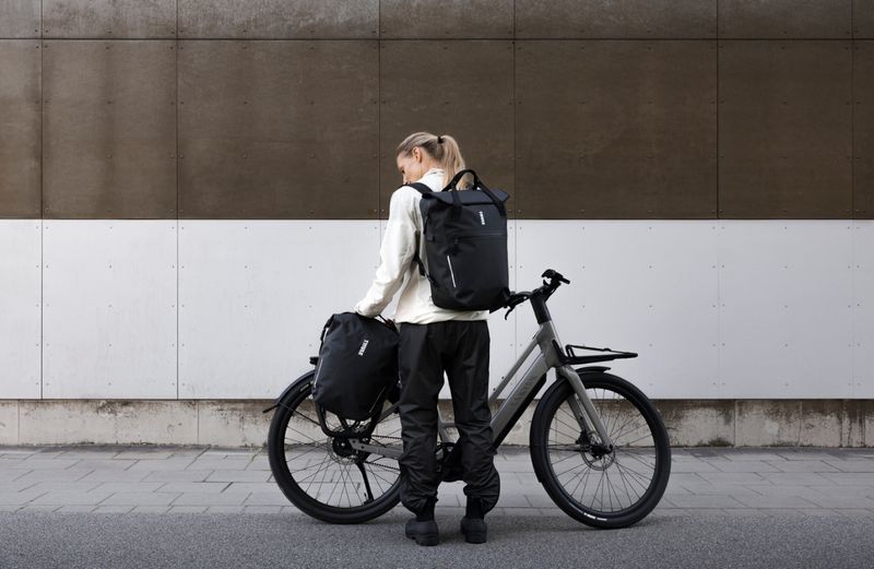 Um ciclista está em frente a uma bicicleta elétrica cinzenta montada no sistema de alforges InLock da Thule, juntamente com dois sacos pretos Thule Shield.