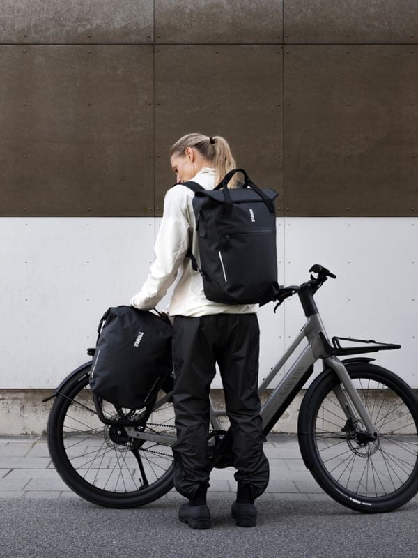 Un cycliste se tient devant un vélo électrique gris équipé du système de sacoches InLock de Thule, accompagné de deux sacs noirs Thule Shield.