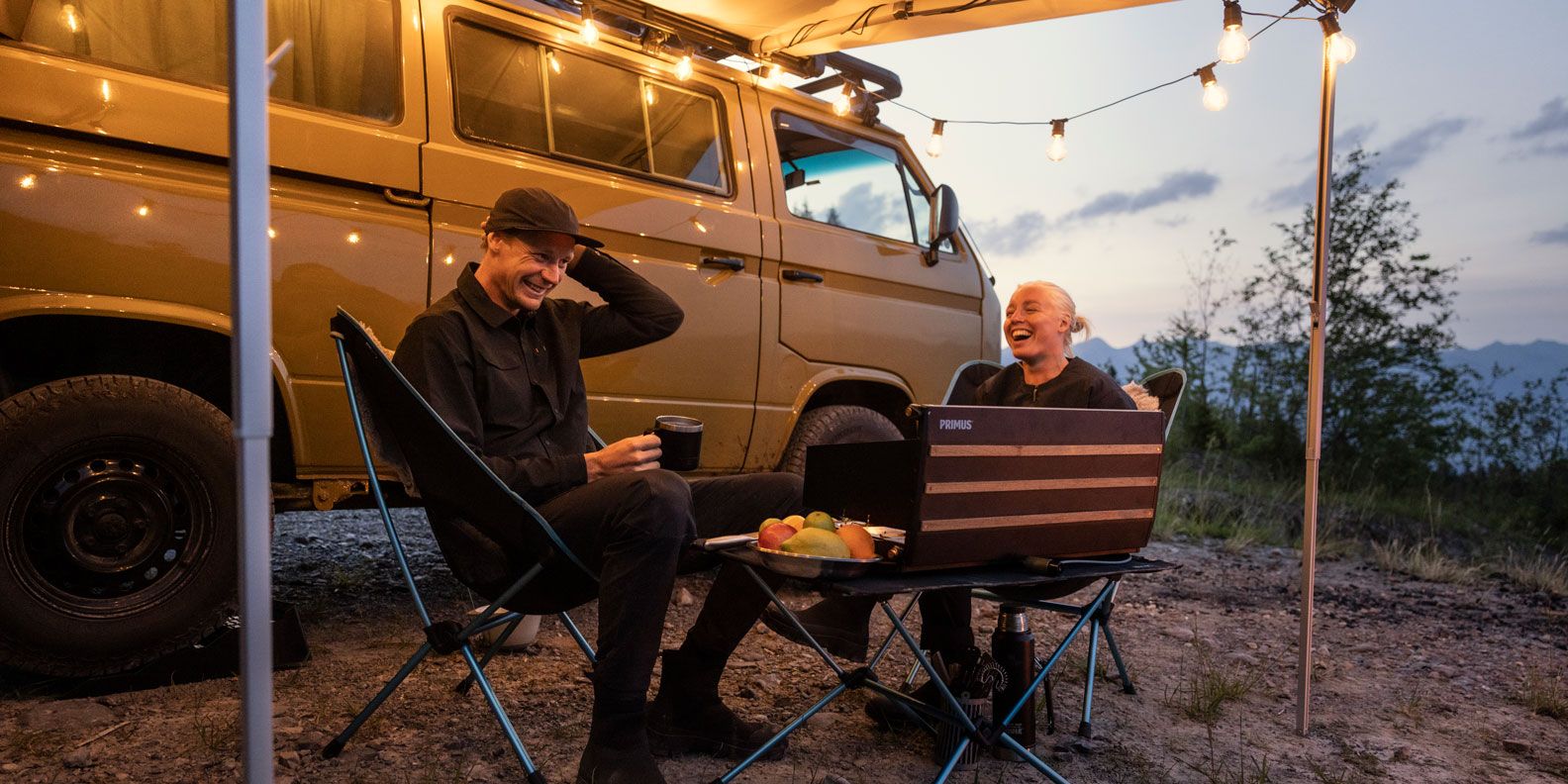 A man and woman sit at sunset under the compact van awning Thule Sidehill.