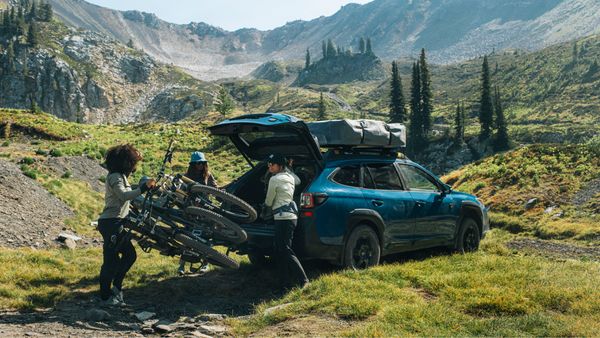A car is parked among the mountains with a rooftop tent, bike racks, bike trailers and more.
