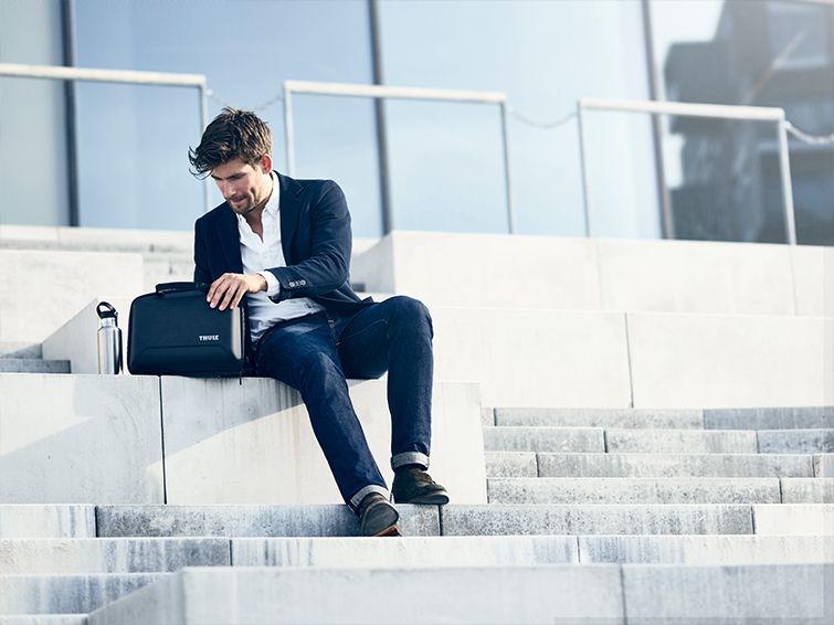 A man in a suit sits on white stairs outdoors opening a laptop case.
