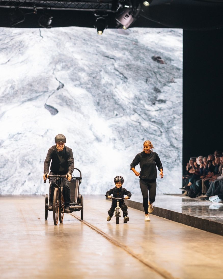 A person biking on a runway with a child riding a small bike beside them during a show.