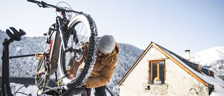Xavier De Le Rue attaches his winter MTB bike to a Thule bike rack with snowy mountains in the background.