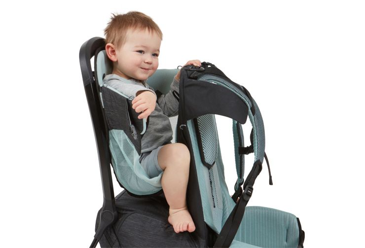 A child sits in a Thule Sapling baby carrier backpack with an ErgoRide seat.