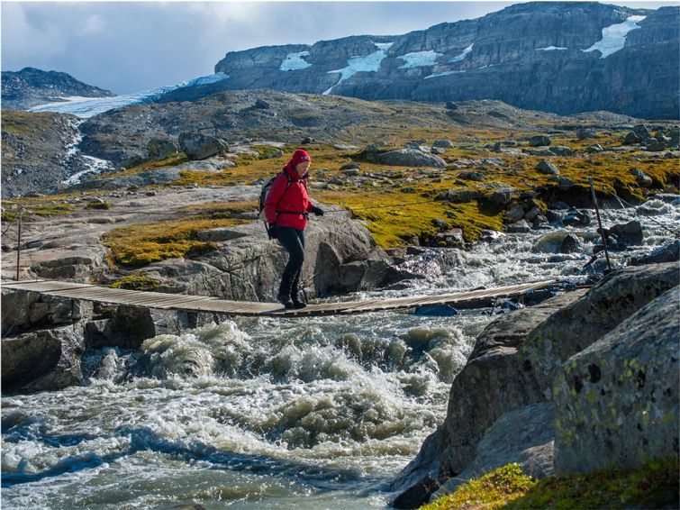 A person in a red coat walks over a creek in the Hardangervidda National Park near Kongsberg.