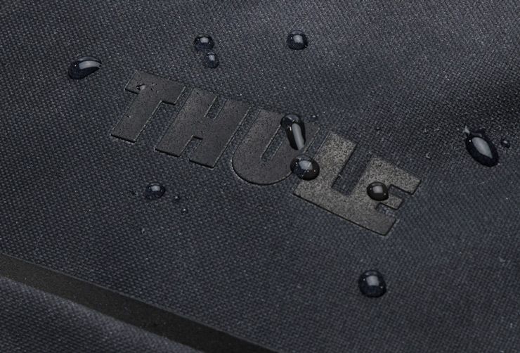 Close-up of water droplets on the black cotton polyester canvas of the Thule Aion travel backpack.