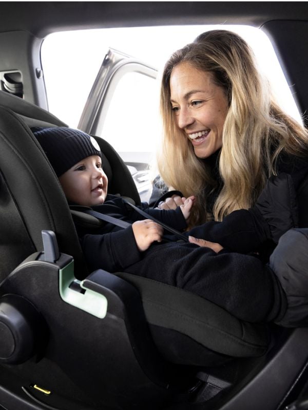 A smiling mother interacts with her baby, who is securely fastened in a Thule car seat inside a vehicle.
