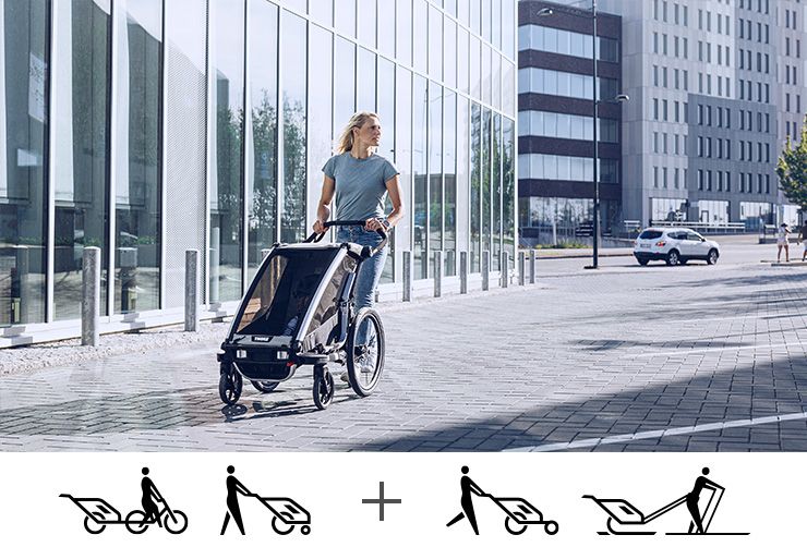 Woman walks with a Thule Chariot Lite bike trailer through city streets