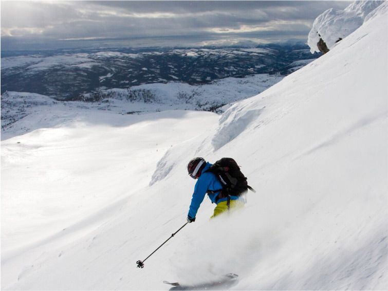 A skier skis down the slopes at Norefjell in Norway with a beautiful view of the expansive landscape below.