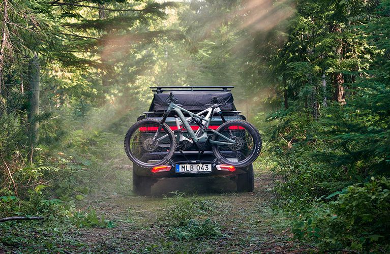 A vehicle is parked in the sunny forest with a Thule Epos bike rack.