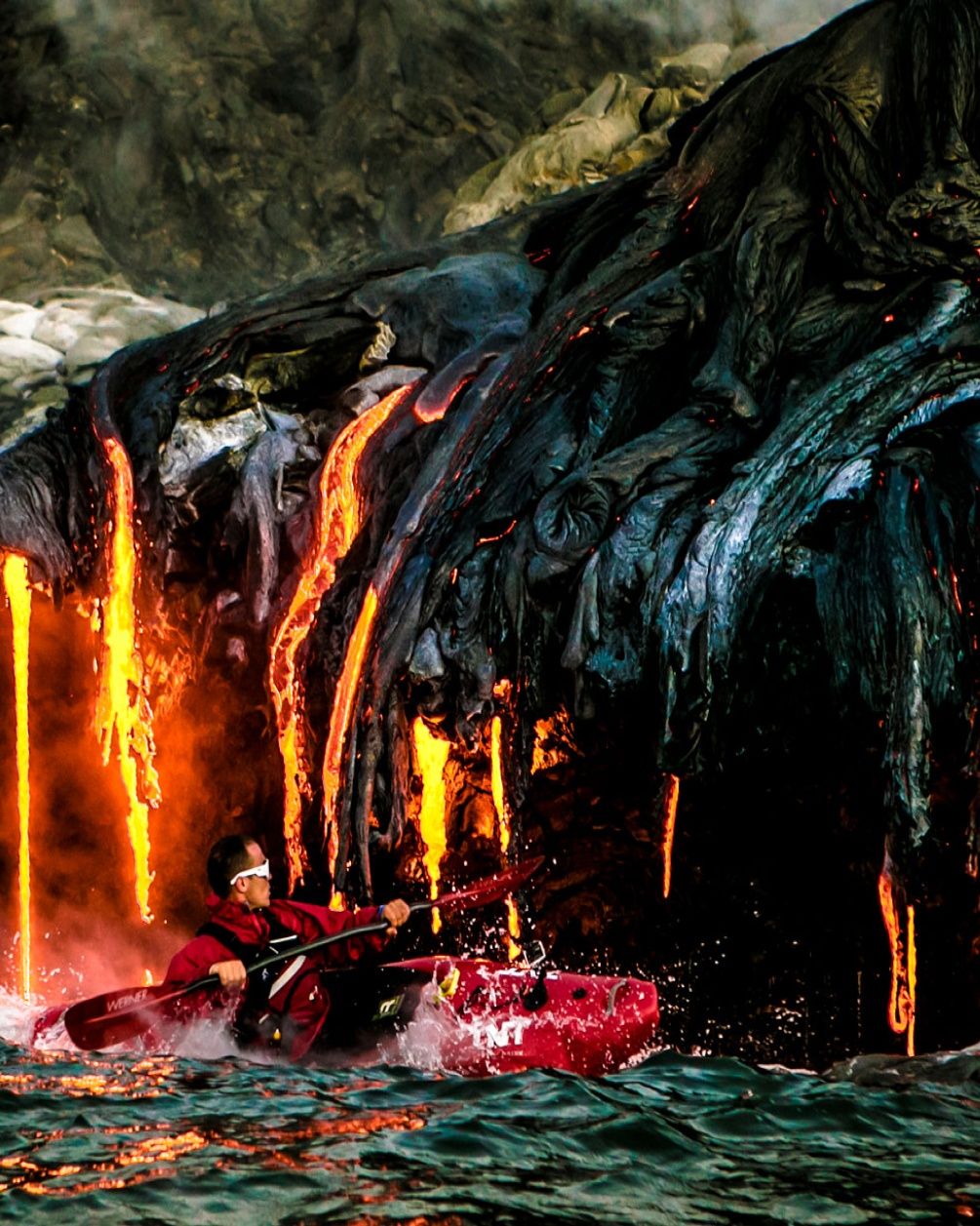 A close up image of Pedro Oliva kayaking in the water with hot lava in the background.