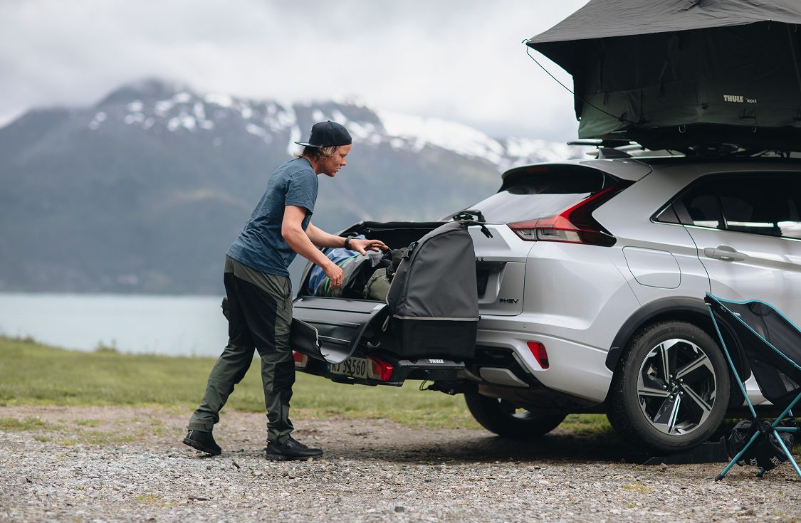 Osoba ładująca sprzęt na tył samochodu wyposażonego w Thule Onto, zaparkowanego w górskim krajobrazie.
