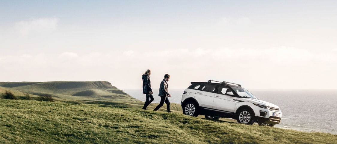 Two people on the countryside walking towards a white car with Thule roof racks.