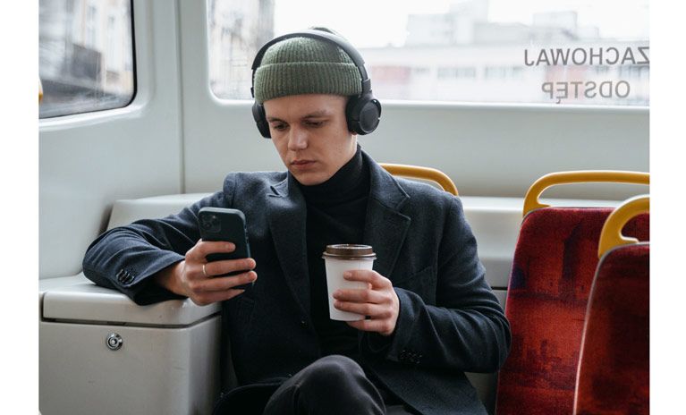 A commuter sits on a bus with a coffee in one hand and his phone in the other.