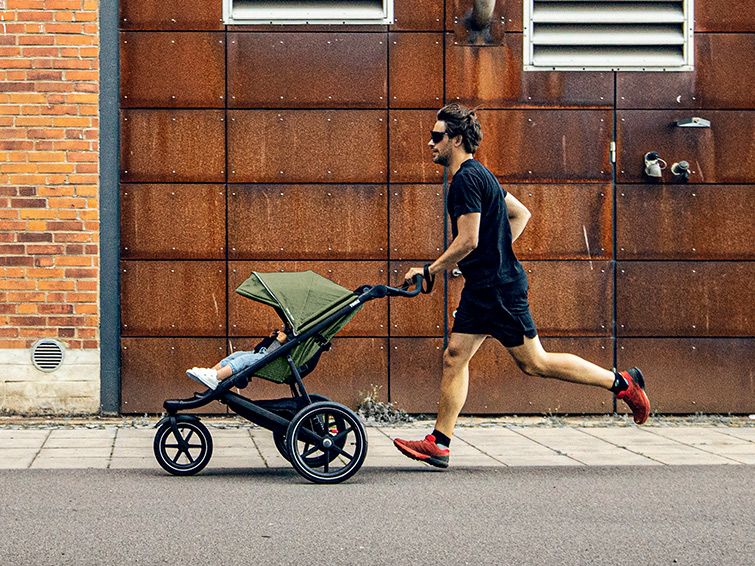 A man runs down a city street with his child in a running stroller.