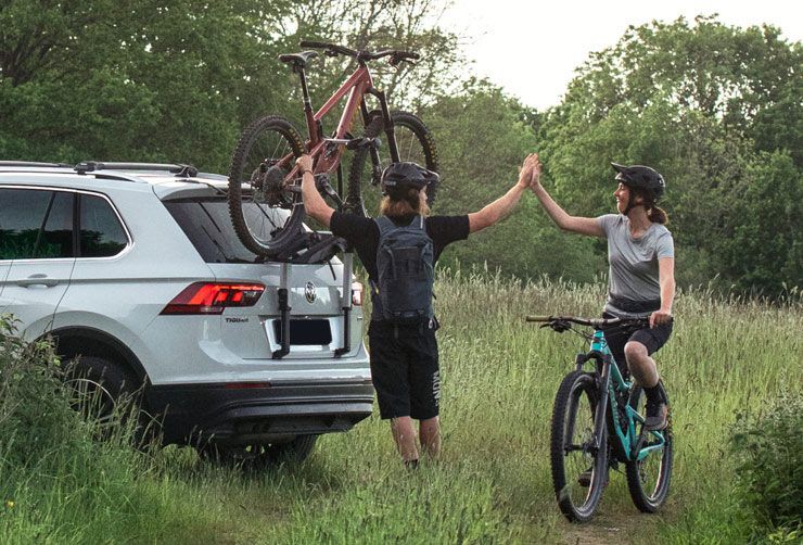 Two cyclists high five as one of them unloads their bike from a Thule trunk bike rack.