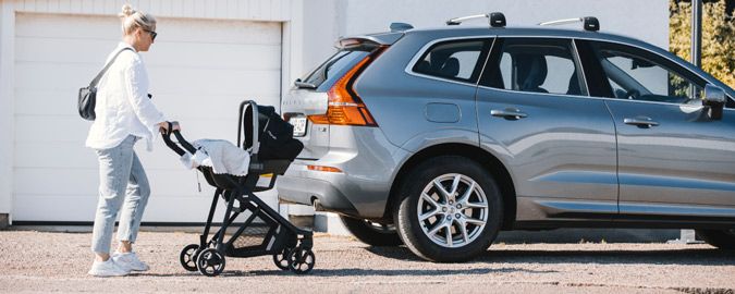 A woman pushes her Thule Shine newborn stroller with a car seat towards her parked car.