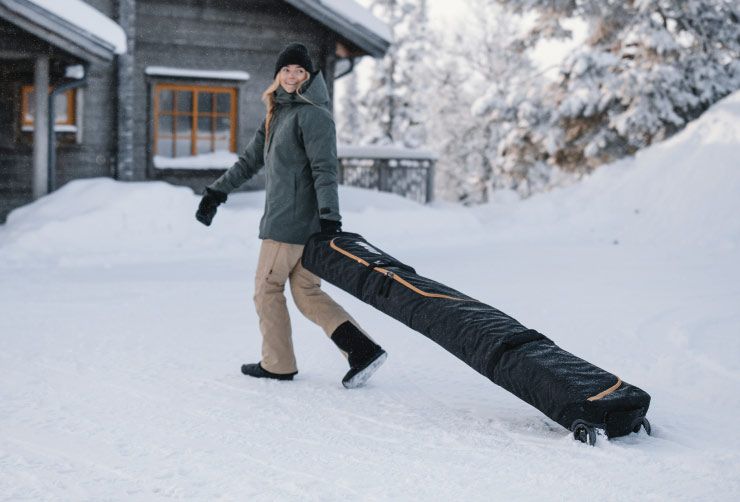 A woman walks through the snow with a Thule RoundTrip ski travel bag.