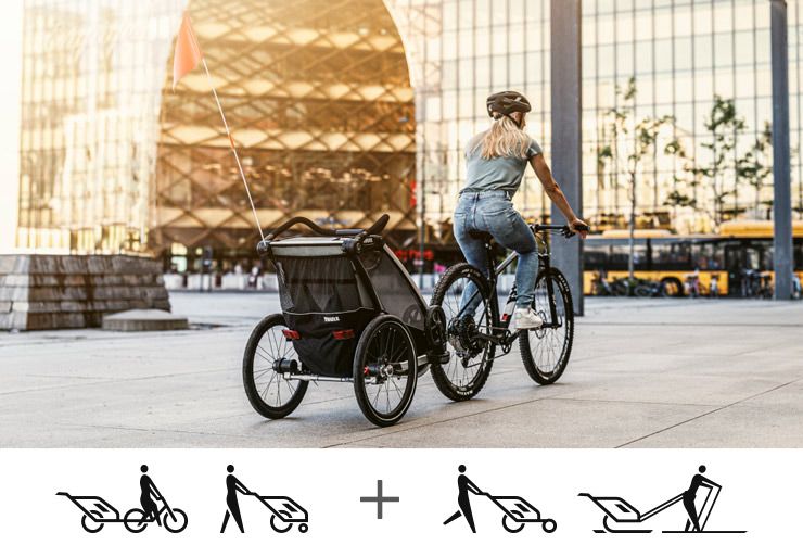 A woman bikes in the center of a busy city with a Thule Chariot Lite bike trailer.