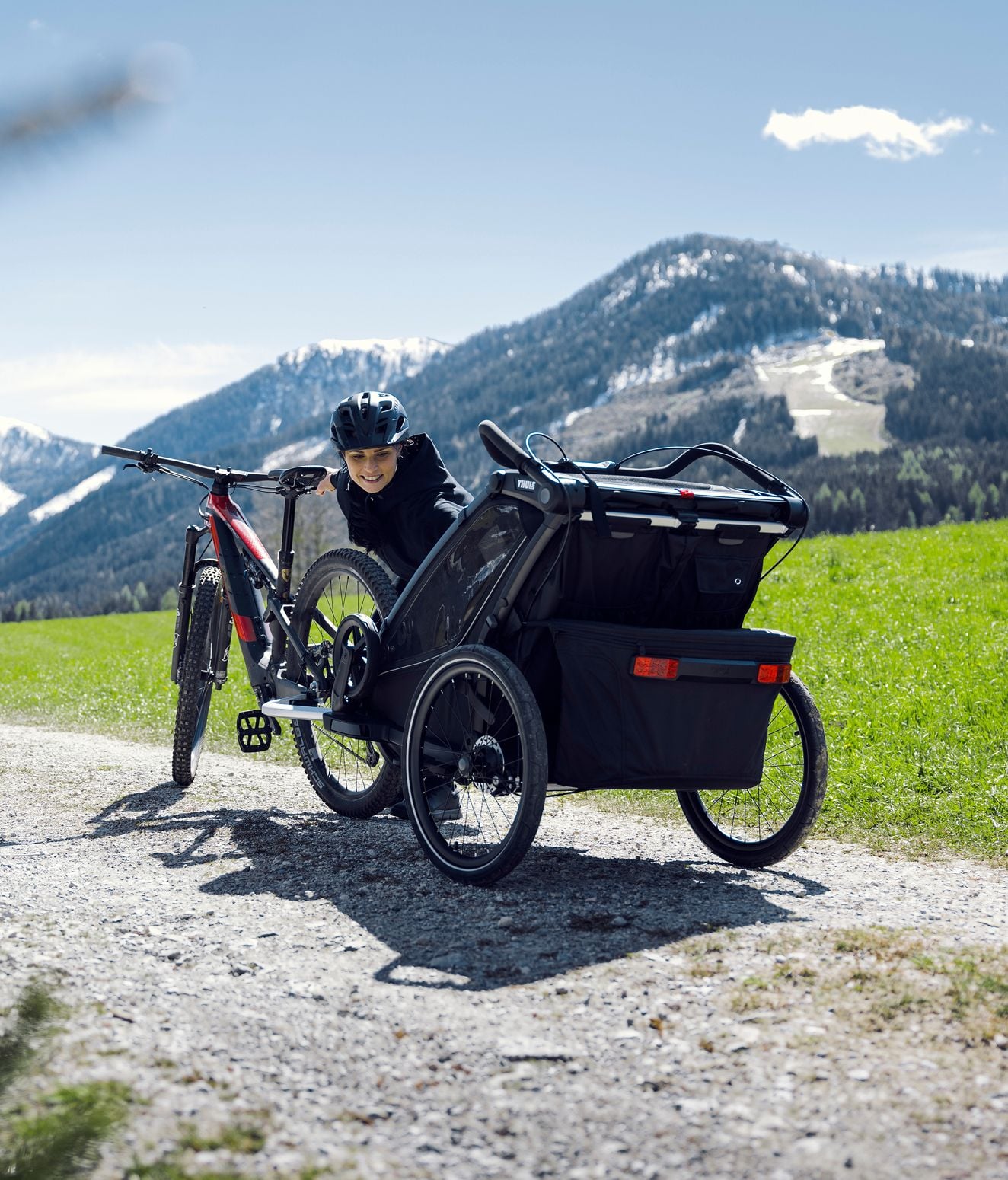 Person, die neben einem Fahrrad mit Fahrradanhänger steht und mit einem Kind interagiert.