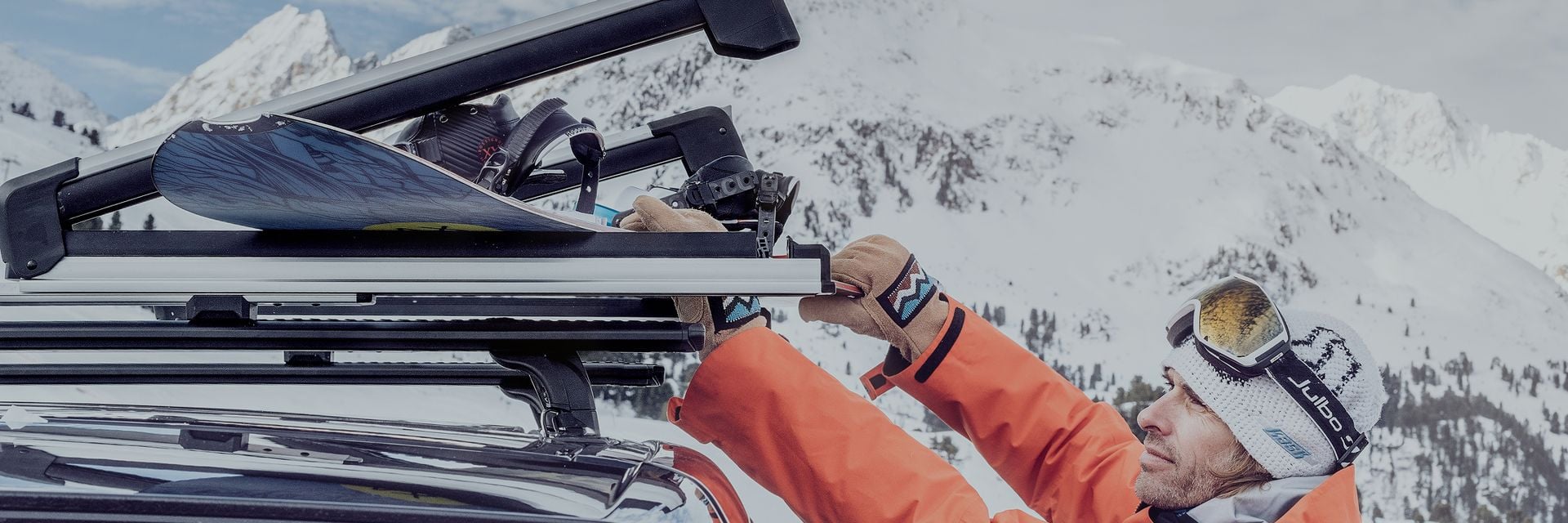 Thule Outlet hero banner showing a skier loading gear onto a roof rack in a snowy mountain landscape.