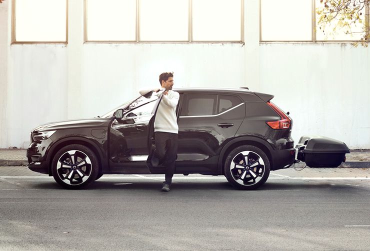 一个男人从电动车上下来，车尾安装有拖车箱。