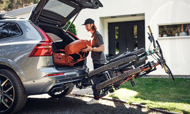 A man accesses his trunk while the Thule Easy Fold XT towbar bike rack still have the bikes loaded.