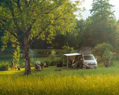 Asuntoauto, jossa on Thule Subsola -markiisipaneelit, luoden suojaisan ulkotilan järven rannalle.