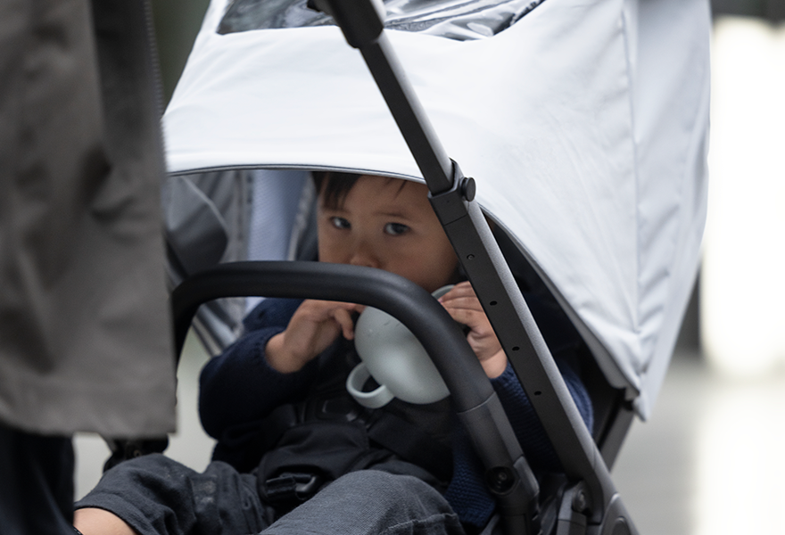 A toddler sits inside the Thule Shine Air Purifier Canopy taking a sip from a sippy cup.