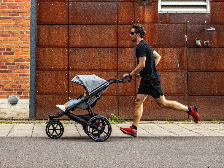 A man runs down a city street with his child in a running stroller.
