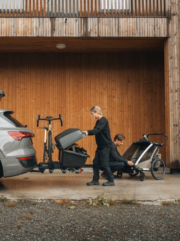 En förälder säkrar en cykel på en Thule Santu förvaringslösning fäst på en dragkroksmonterad cykelhållare baktill på en SUV.