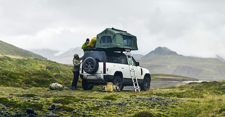 A Thule car top tent is parked in misty fields and two people fill it with gear.